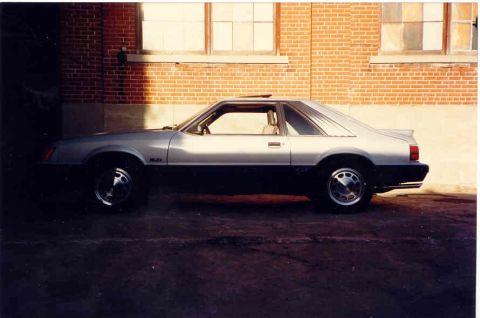 1967 Ford Fairlane - Side profile of a two-tone Ford Mustang with a sunroof, parked in front of a brick wall.