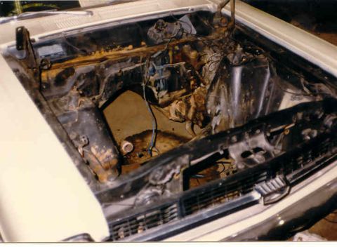 1967 Ford Fairlane - The engine bay of a white car shows significant rust and disarray, with the engine removed.