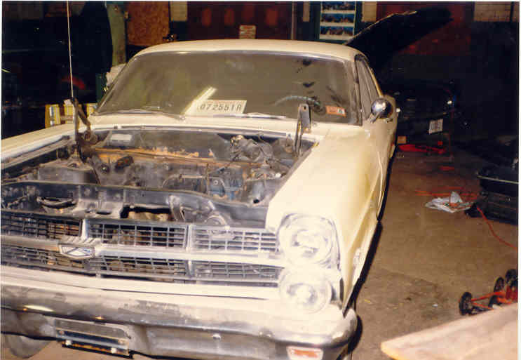 Cream Ford Fairlane in a shop with hood off and engine bay stripped