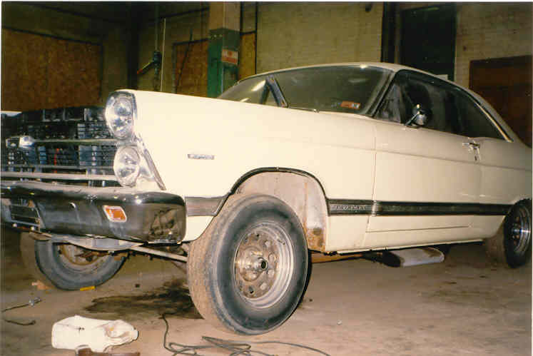 Cream Ford Fairlane hardtop mid-teardown in a shop with grille removed