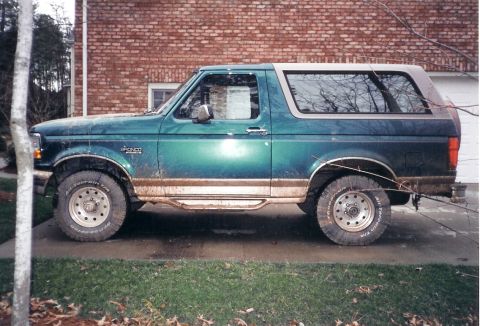 1996 Ford Bronco - A green 1996 Ford Bronco is parked on a concrete driveway in front of a brick building.