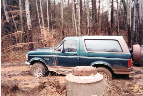1996 Ford Bronco - A 1996 Ford Bronco navigates a muddy trail in a wooded area.