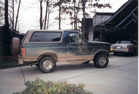 1996 Ford Bronco - A dirty Ford Bronco is parked in a driveway with a convertible behind it.