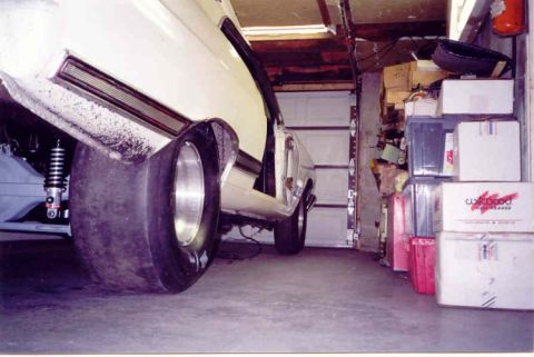 1967 Ford Fairlane - A car with large rear tires is parked inside a cluttered garage with a garage door in the background.