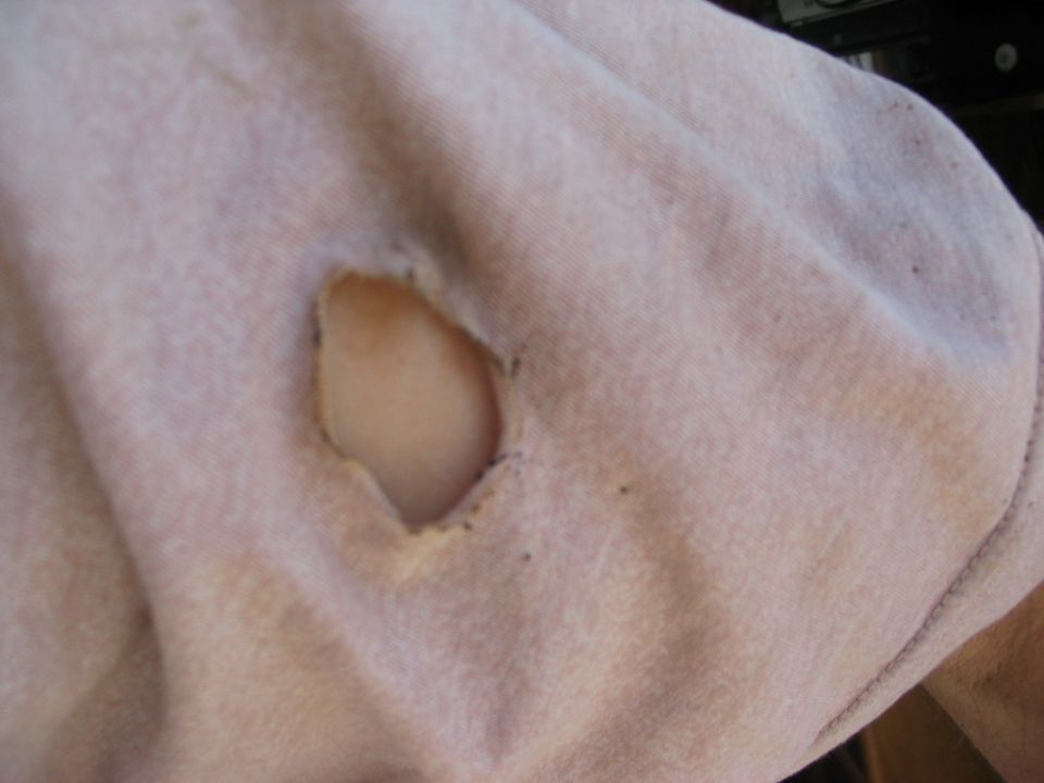 Close-up of oval hole cut in tan cloth vehicle upholstery with frayed edges