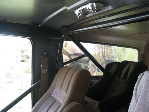 1986 Ford Bronco - Vehicle interior a roll cage and aftermarket seats, with a towel on the passenger seat.