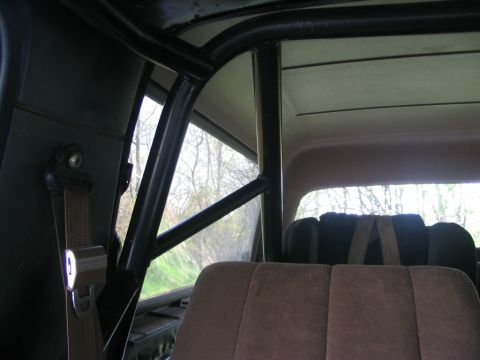 1986 Ford Bronco - The interior of a vehicle is shown with a prominent roll cage and seatbelts.