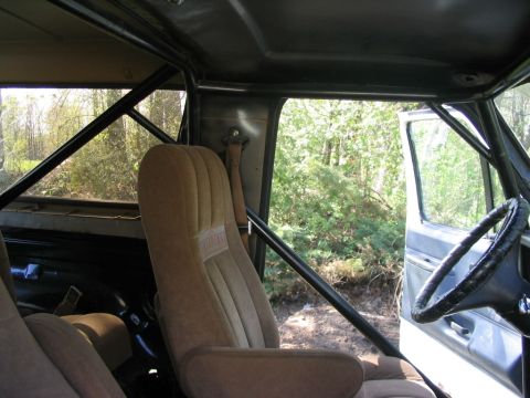1986 Ford Bronco - The interior of a vehicle is shown with tan seats and a prominent roll cage, with trees visible through the open door.