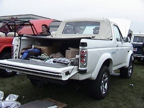 1995 Ford Bronco - A white Ford Bronco is parked with its tailgate open, revealing a load of items inside. Another Bronco is parked nearby.