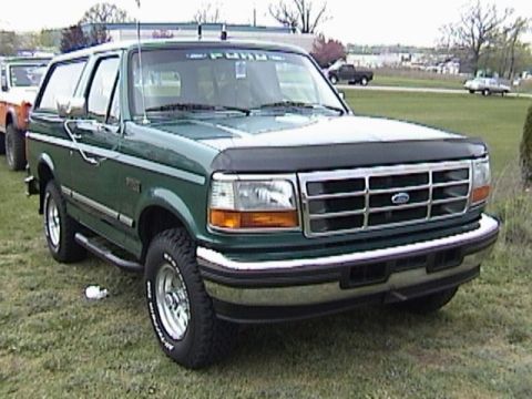 1995 Ford Bronco - A green Ford Bronco is parked on a grassy field next to another vehicle.