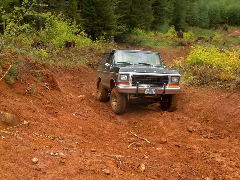 1978 Ford Bronco - A 1978 Ford Bronco navigates a steep, muddy incline on a wooded trail.