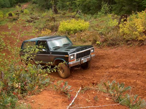 1978 Ford Bronco - A 1978 Ford Bronco navigates a muddy, wooded trail, kicking up red dirt.