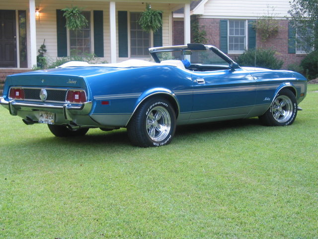 Blue 1973 Ford Mustang convertible parked on grass in front of a house, rear quarter view