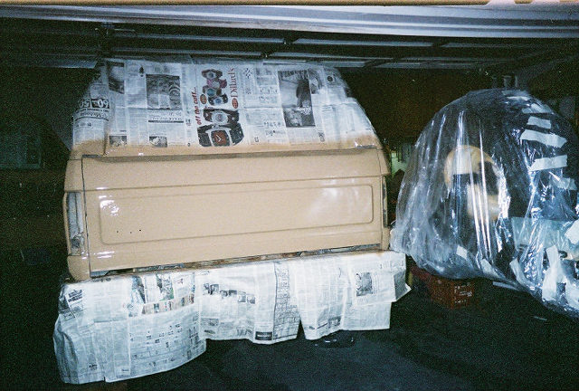 Tan painted tailgate and parts drying on newspaper-covered surface in dim garage
