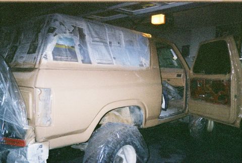 1983 Ford Bronco - A tan Ford Bronco is undergoing a paint job, with its windows taped and tires covered.