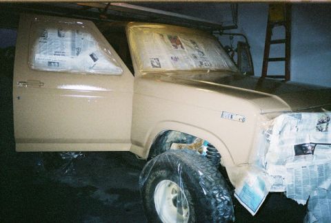 1983 Ford Bronco - A tan 1983 Ford Bronco is shown with its door open and windows taped off, indicating it is in the process of being painted.