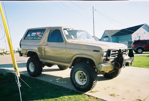 1983 Ford Bronco - This lifted Ford Bronco has a custom front bumper and off-road tires, with a red SUV parked in the background.