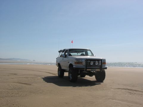 1995 Ford Bronco - White 1995 Ford Bronco parked on a sandy beach with the ocean in the background.
