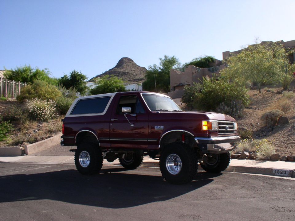 Maroon lifted 1990 Ford Bronco with chrome wheels parked on asphalt