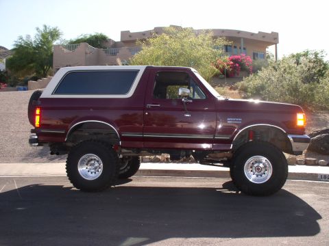 1990 Ford Bronco - This lifted Ford Bronco is shown from the side, with a house and landscaping in the background.