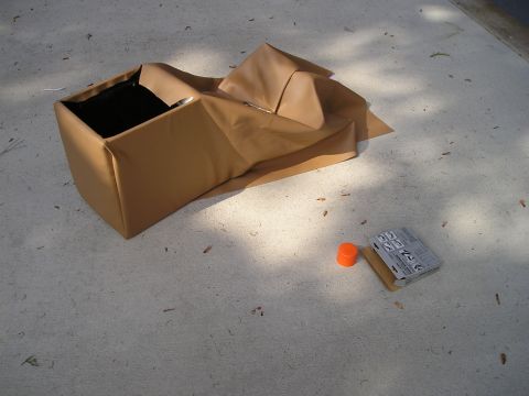 1996 Ford Bronco - A tan center console with a black interior sits on a concrete surface, accompanied by an orange cap and a small box.