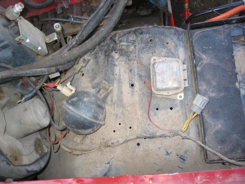 1985 Ford Bronco - Close-up view of engine bay components, including a voltage regulator and a black vacuum ball, with visible wiring and hoses.
