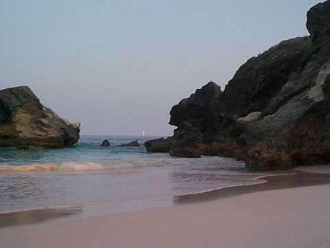 1994 Ford Bronco - A tranquil beach scene unfolds with rocky outcrops and the calm sea, a lone sailboat dots the horizon.