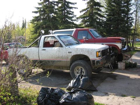 1985 Ford Bronco - Two pickup trucks, a white one and a red Ford Bronco, are parked outside.