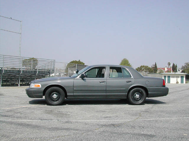 Gray Ford Crown Victoria police car parked on asphalt, side view