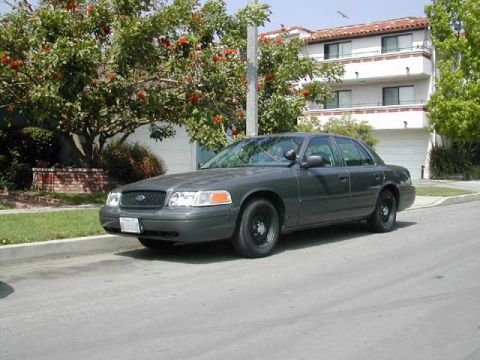 2000 Ford Crown Victoria - 2000 Ford Crown Victoria sedan parked on a residential street with a building in the background.
