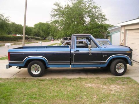 1984 Ford F-150 - Side view of a blue and black 1984 Ford F-150 pickup truck parked in front of a garage.