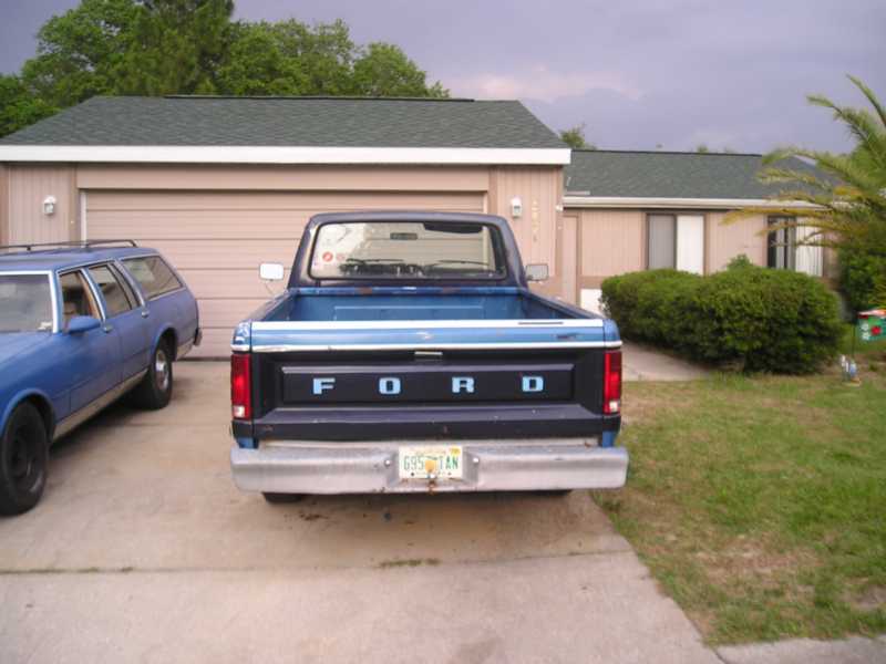 Blue Ford pickup truck rear view, with 'FORD' spelled out on tailgate. License plate visible