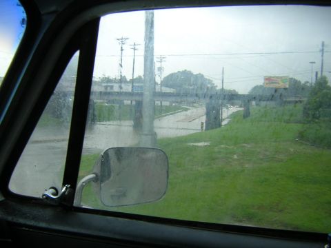 1984 Chevrolet Blazer - The scene shows a flooded road and surrounding area, viewed through a vehicle's side window during inclement weather.