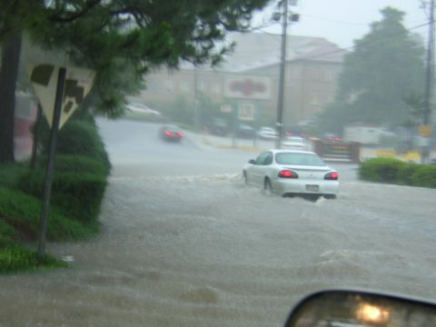 1984 Chevrolet Blazer - A white sedan navigates through flooded streets during a downpour, with another vehicle visible further ahead.