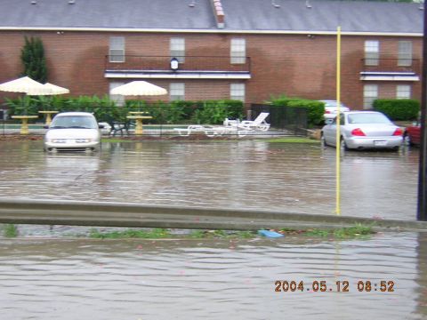 1984 Chevrolet Blazer - Two cars are partially submerged in floodwaters outside an apartment complex on a cloudy day.