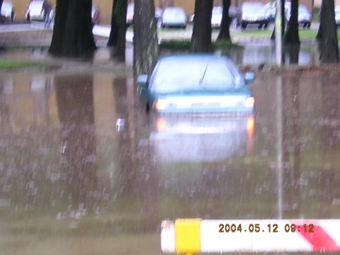 1984 Chevrolet Blazer - A teal sedan is submerged in floodwaters on a street with trees and other vehicles in the background.