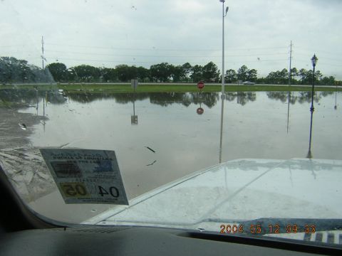 1984 Chevrolet Blazer - A vehicle is partially submerged in floodwaters on a cloudy day, with trees and streetlights reflected in the water.