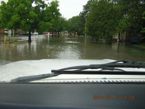 1984 Chevrolet Blazer - A street is flooded with water, with several vehicles visible in the background, some partially submerged.