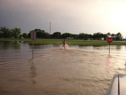 1984 Chevrolet Blazer - A person wades through a flooded road after heavy rains, with a stop sign visible.