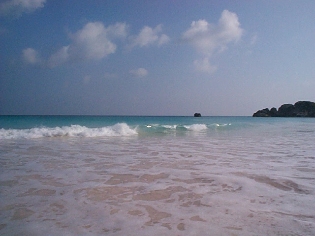 Ocean waves on a sandy beach with clouds in the sky and rocks in the distance