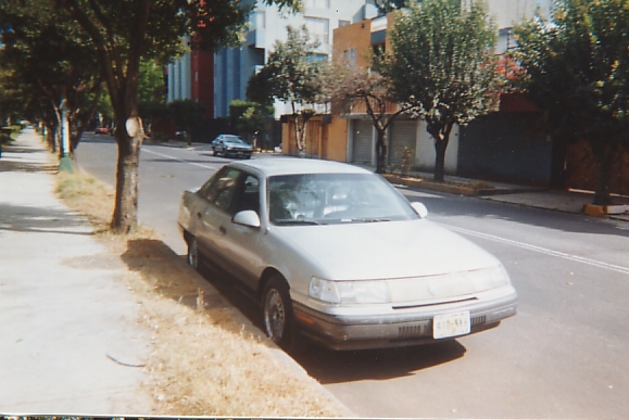 Silver sedan parked curbside on a tree-lined city street, front three-quarter view