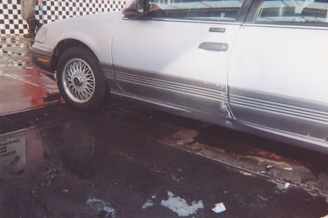1991 Ford Taurus - This silver sedan shows damage to its lower body panel and features a multi-line pinstripe detail along the side.