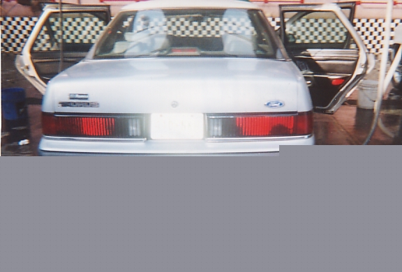 Rear of a silver Ford sedan parked in a shop with checkered backdrop