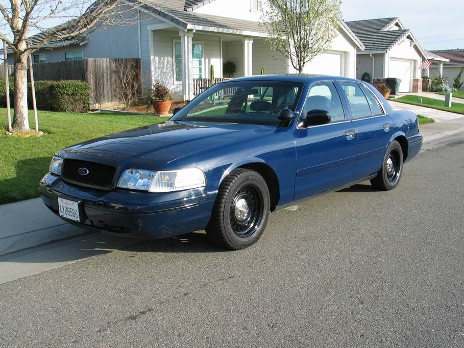 Dark blue Ford Crown Victoria sedan with steel wheels parked on a residential street