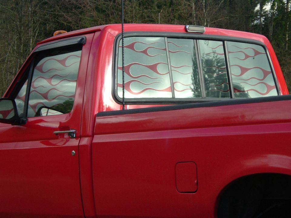 Red pickup cab side view with flame-pattern graphic on the rear sliding window