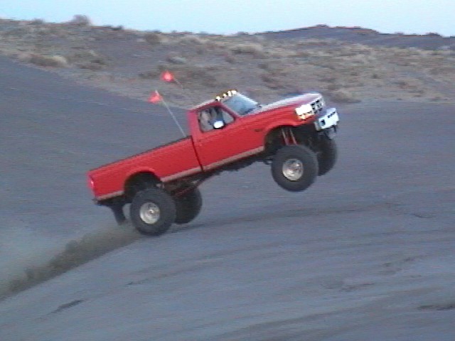 Red lifted Ford pickup catching air over a dirt dune off-road