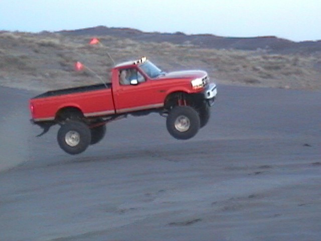 Red lifted Ford pickup jumping with all four wheels off the ground on sand dunes