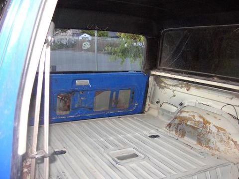 1980 Ford Bronco - The interior of a vehicle, possibly a truck or SUV, shows a blue door panel and a white, ribbed cargo area.