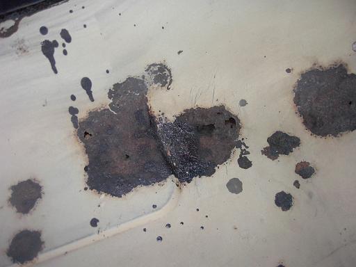 Close-up of rust patches and dark splatter on cream painted body panel