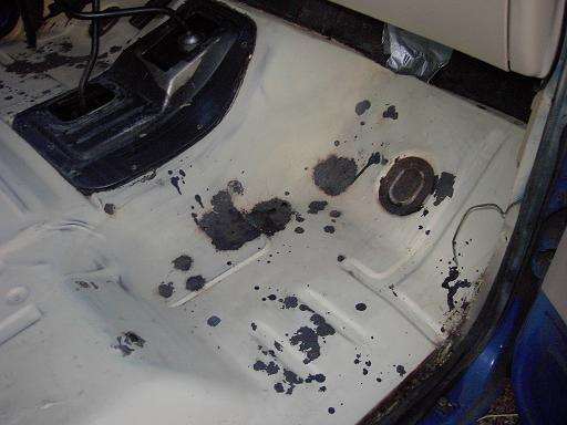 Bare white-painted truck floor pan with black patch coating during interior restoration